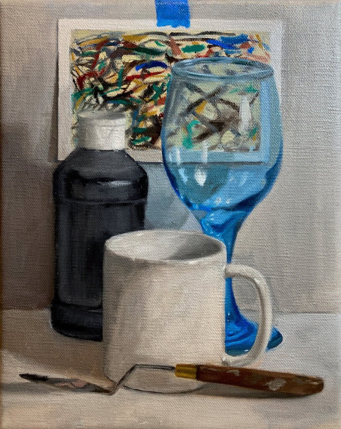 still life painting of a post card, blue wine glass, black paint bottle, white coffee mug and a palette knife