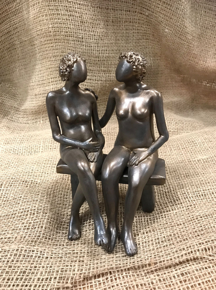 Two women sitting on a bench painted in bronze coloring, made of clay.